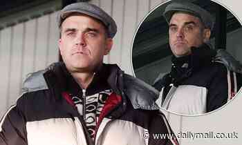 Robbie Williams keeps off the winter chill in a jacket as he enjoys Port Vale football match