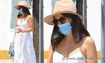Camilla Belle cuts a chic figure in a stylish white summer dress as she covers up in a face mask