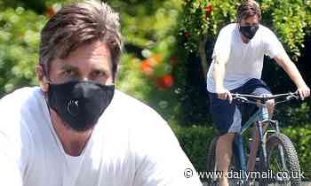 Christian Bale covers up in a black reusable face mask as he heads out for a solo bike ride