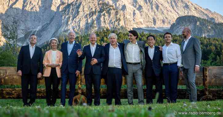 Gipfelteilnehmer posieren vor berühmter Holzbank