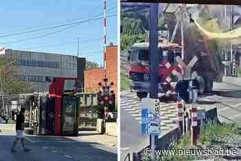 Beelden tonen hoe vrachtwagen met laadbak omhoog bovenleiding afrukt en kantelt op overweg, treinverkeer onderbroken