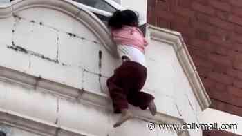 Moment young girl clings to window ledge above London shop before falling into arms of a man and police officer below