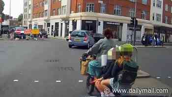 Moment woman cyclist with THREE children riding on back pedals through a red light and holds up her hand to try and stop cars as she dodges traffic