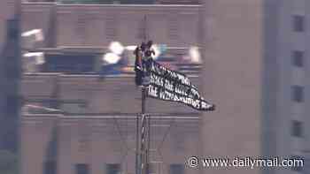 Wild scene as masked pair scales Empire State Building to very top and fly banner about love and peace