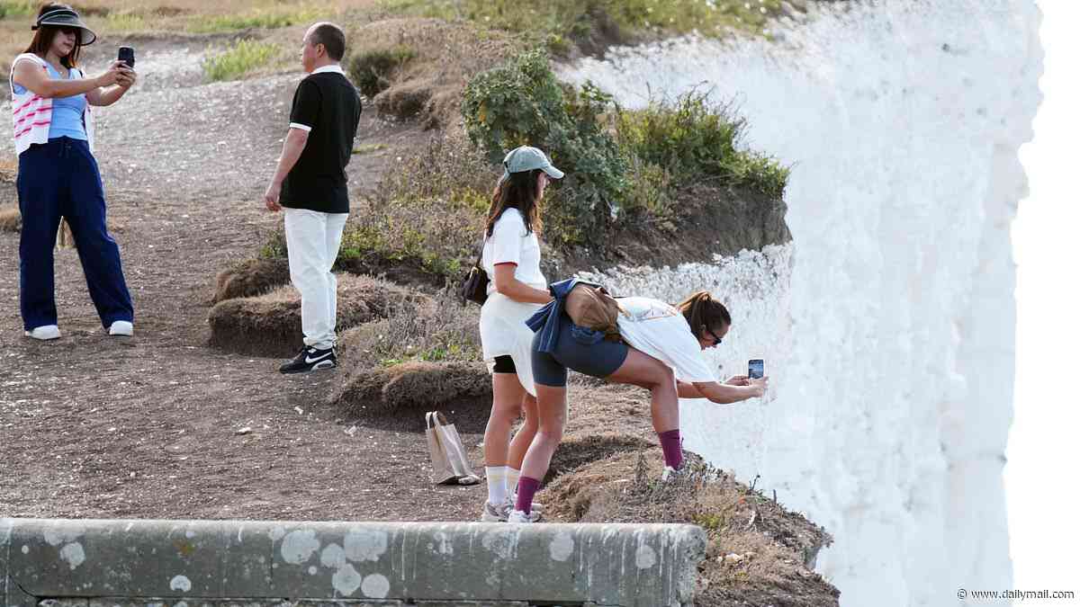Selfie-loving tourists ignore warning signs as they hop over safety railings to pose perilously close to 500ft drop at Birling Gap