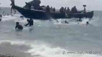 Sunbathers look on in shock as packed migrant boat arrives on Spanish beach and dozens of men run ashore and disappear