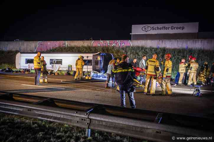 Touringcar rijdt door vangrail en belandt op zijn zijkant