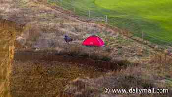 That's no place to pitch your tent! 'Idiot' climbs fence and ignores warning signs to set up camp on edge of crumbling 150ft seaside cliff