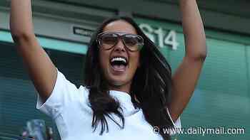 Maya Jama delightedly throws her hands in the air and flashes a glimpse of her midriff as she cheers on the teams at the Women's Super League football match