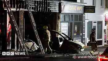 Flats evacuated as car hits shopfront and catches fire