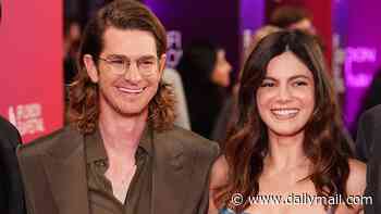 Andrew Garfield tucks his long locks behind his ears as he beams alongside girlfriend Monica Barbaro at the BFI London Film Festival premiere of Artificial