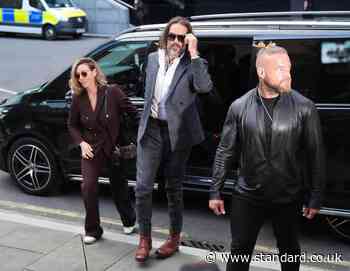 Russell Brand flanked by security as he arrives at London court for rape and sex assault trial